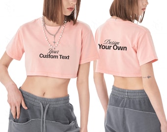 Może przedstawiać: Jasnoróżowy crop top z napisem "Your Custom Text" z przodu i "Design Your Own" z tyłu. Koszulka jest połączona z szarymi spodniami dresowymi. Noszony jest naszyjnik.