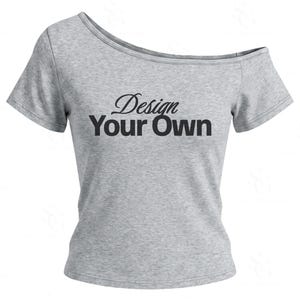 Könnte beinhalten: Ein graues, meliertes T-Shirt mit schulterfreiem Ausschnitt und dem schwarzen Schriftzug Design Your Own auf der Brust. Das Kleidungsstück hat kurze Ärmel und einen weiten, asymmetrischen Halsausschnitt, der über einer Schulter liegt.