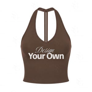 Puede incluir: Un top corto de color marrón oscuro estilo halter con un escote en V profundo y tirantes estilo nadador. La parte delantera de la prenda muestra el texto blanco "Design Your Own", con la palabra "Design" en cursiva y "Your Own" en negrita.