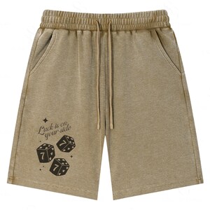 May include: Tan-colored shorts with a drawstring waist and pockets. The shorts feature the text "Luck is on your side" and three dice with the number seven. The shorts are made of a soft, comfortable material.