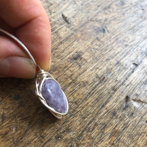 May include: A silver wire wrapped pendant featuring a purple gemstone.
