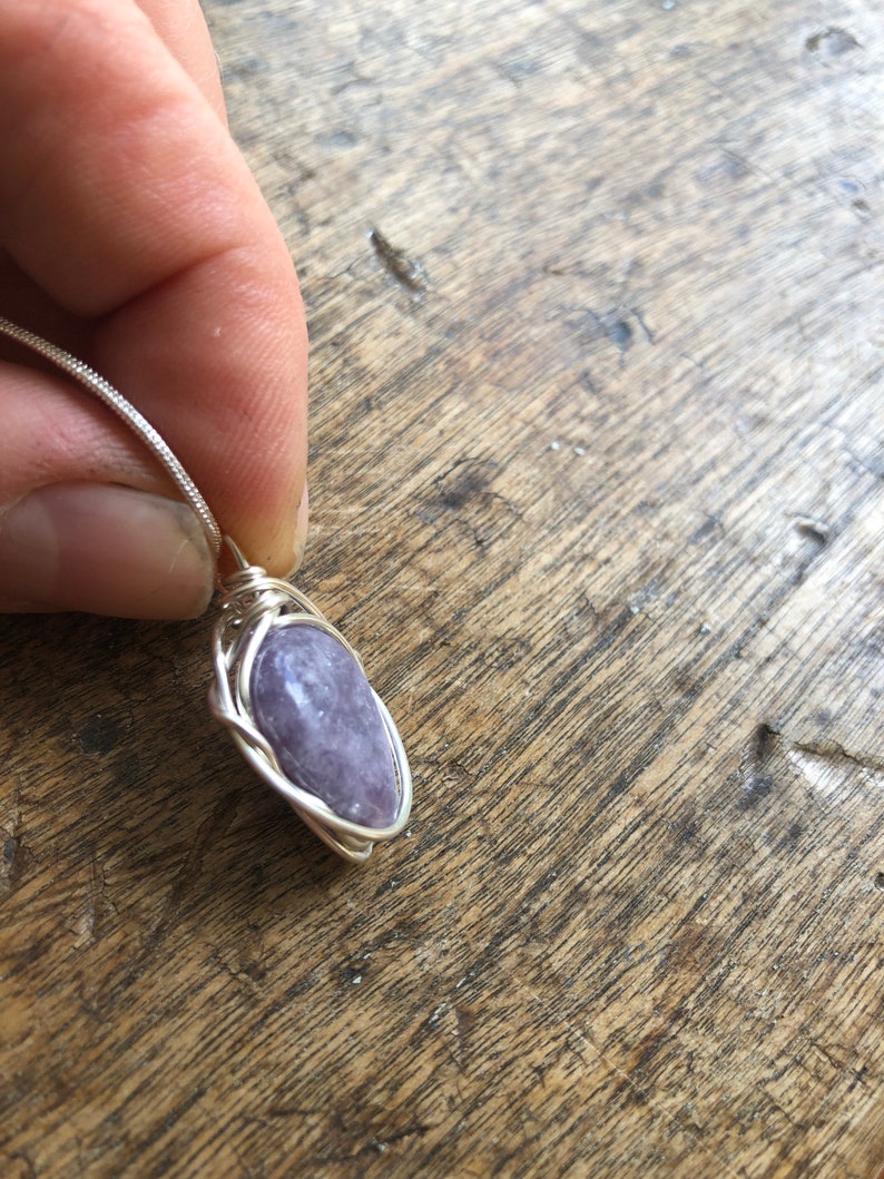 May include: A silver wire wrapped pendant featuring a purple gemstone.