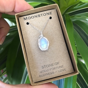 May include: A silver chain necklace with a moonstone pendant wrapped in silver wire. The necklace is in a small box with the words "Moonstone" and "Stone of Good Fortune Business - Love" printed on it.