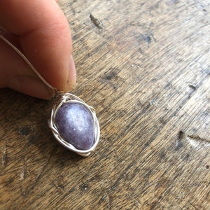 May include: A silver wire wrapped pendant featuring a purple gemstone. The pendant is hanging from a silver chain.