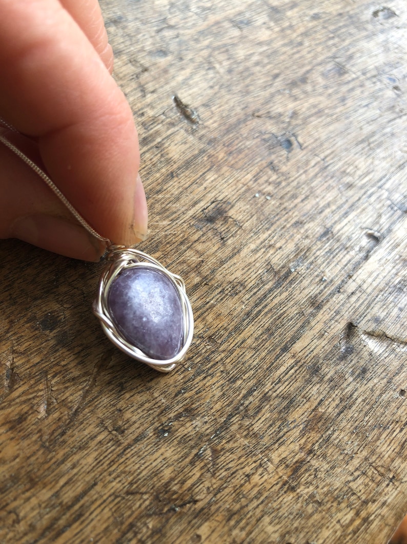 May include: A silver wire wrapped pendant featuring a purple gemstone. The pendant is hanging from a silver chain.