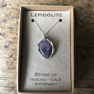 Peut inclure: Un collier en chaîne argent avec un pendentif en pierre de Lepidolite violette enveloppé de fil d'argent. Le pendentif est dans une petite boîte avec le texte "Lepidolite" et "Pierre de guérison - Calme Anti-Anxiété".