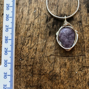 May include: A silver chain necklace with a purple gemstone pendant wrapped in silver wire.