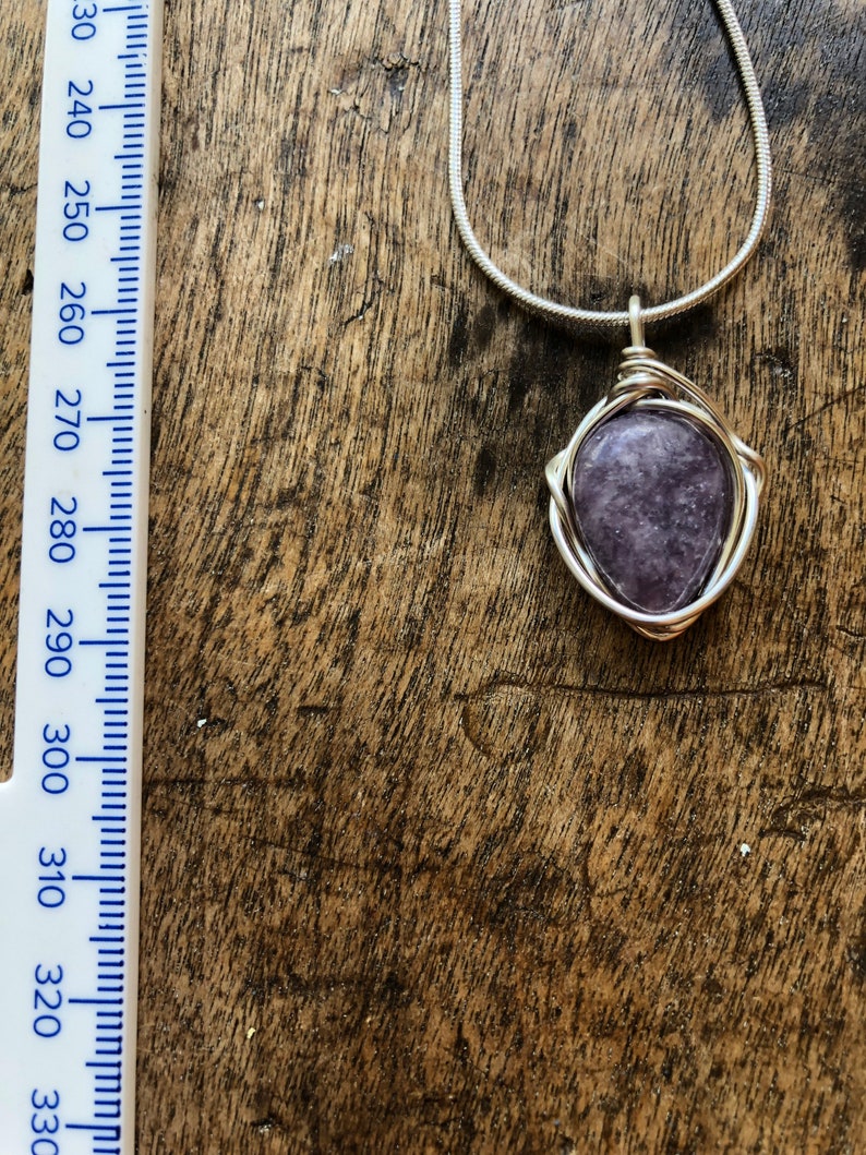 May include: A silver chain necklace with a purple gemstone pendant wrapped in silver wire.