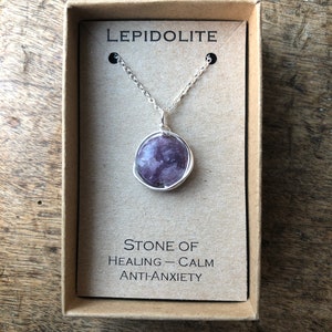 Peut inclure: Un collier en chaîne argent avec un pendentif en pierre de lépidolite violette. Le pendentif est enveloppé de fil d'argent. Le collier est dans une boîte brune avec les mots "Lepidolite" et "Pierre de guérison - Calme Anti-Anxiété".