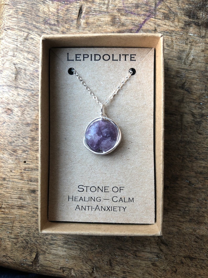 Pu&ograve; includere: Una collana a catena d'argento con un ciondolo in pietra di lepidolita viola. Il ciondolo &egrave; avvolto in filo d'argento. La collana &egrave; in una scatola marrone con le parole "Lepidolite" e "Pietra di guarigione - Calma Anti-Ansia".