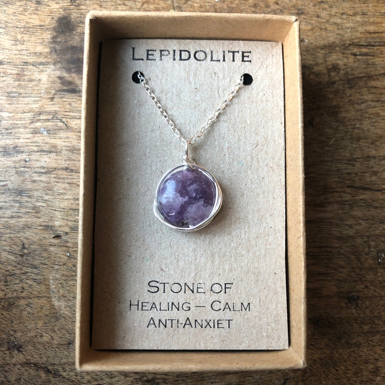 Pu&ograve; includere: Una collana a catena d'argento con un ciondolo in pietra di Lepidolite viola. La pietra &egrave; avvolta in filo d'argento e la collana &egrave; in una piccola scatola con il testo "LEPIDOLITE" e "PIETRA DI GUARIGIONE - CALMA ANTI-ANSIA".