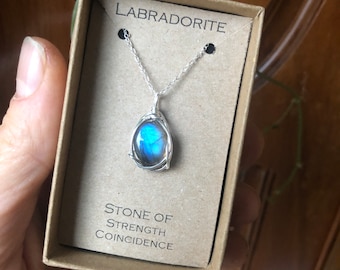 May include: A silver chain necklace with a blue labradorite gemstone pendant. The pendant is wrapped in silver wire and the box says "Labradorite Stone of Strength Coincidence".