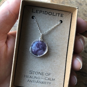 Pu&ograve; includere: Una collana a catena d'argento con un ciondolo rotondo in pietra di lepidolita viola. Il ciondolo &egrave; avvolto in filo d'argento. La collana &egrave; in una scatola con le parole "Lepidolite" e "Pietra di guarigione - Calma Anti-Ansia".
