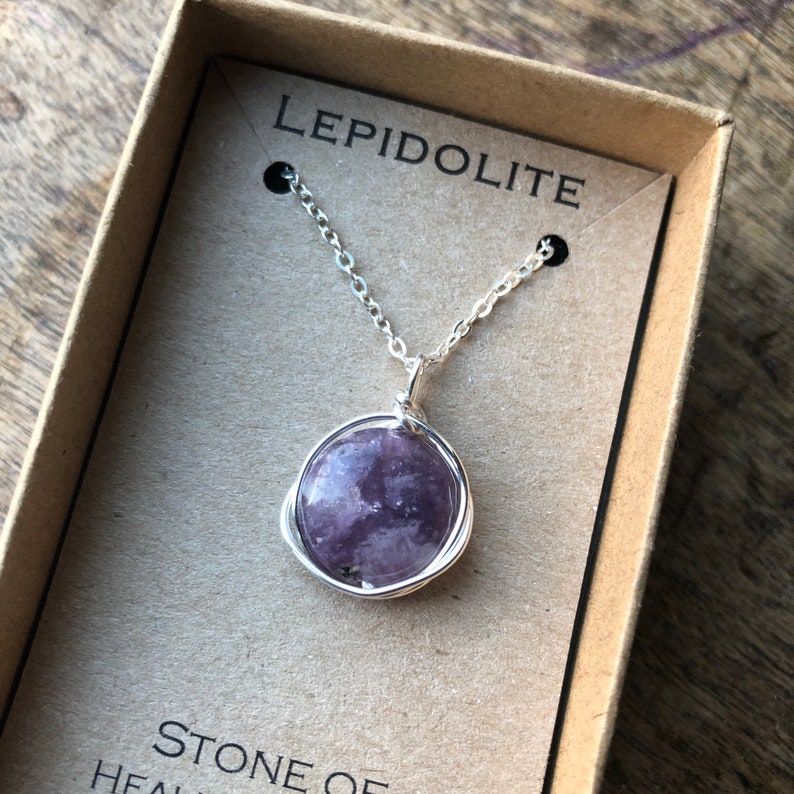 Pu&ograve; includere: Una collana a catena d'argento con un ciondolo rotondo in lepidolita viola. Il ciondolo &egrave; avvolto in filo d'argento. La collana &egrave; in una scatola con le parole "Lepidolite" e "Pietra di guarigione" stampate su di essa.