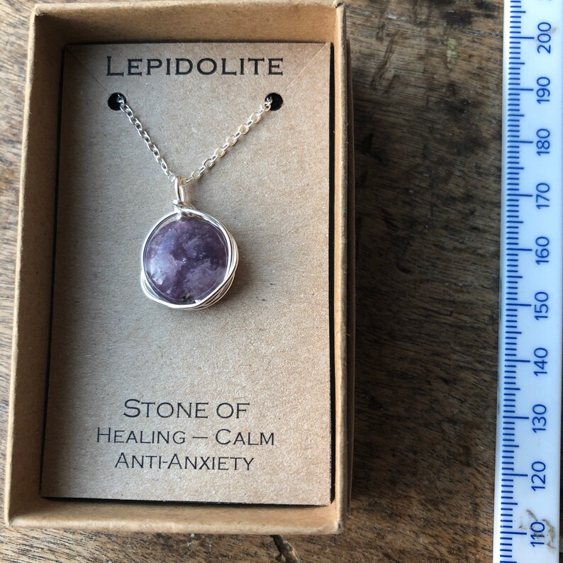 Pu&ograve; includere: Una collana a catena d'argento con un ciondolo rotondo in pietra di lepidolita viola. Il ciondolo &egrave; avvolto in filo d'argento. La collana &egrave; in una piccola scatola con le parole "LEPIDOLITE", "PIETRA DI", "GUARIGIONE - CALMA", e "ANTI-ANSIA" stampate su di essa.