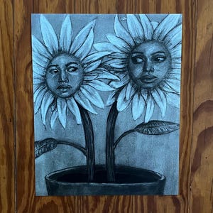 May include: A black and white pencil drawing of two sunflowers with human faces. The flowers are in a black pot, with stems and leaves. The faces have detailed features, with a contemplative expression. The artwork is on a white background.