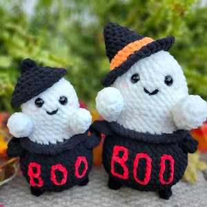 May include: Two handmade crochet ghost figures. The ghosts are white with black eyes and smiles, wearing black hats and dresses. The dresses have the word "BOO" in red. One hat has an orange band.