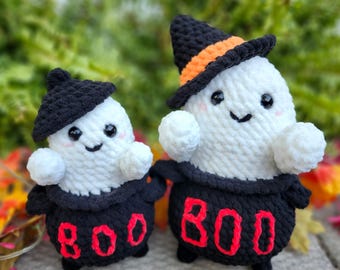 May include: Two handmade crochet ghost figures. The ghosts are white with black eyes and smiles, wearing black hats and dresses. The dresses have the word "BOO" in red. One hat has an orange band.