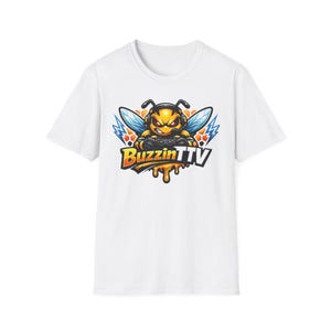 Puede incluir: Camiseta blanca con un diseño de abeja de dibujos animados. La abeja lleva auriculares y sostiene un mando de videojuegos, con el texto "Buzzin TTV". El diseño incluye detalles en naranja, amarillo y azul, con rayos.