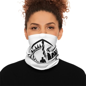 Puede incluir: Cubierta facial blanca con un diseño gráfico negro. El diseño presenta una silueta estilizada de un edificio, una corona y una persona. La cubierta facial se usa alrededor del cuello y cubre la boca y la nariz.