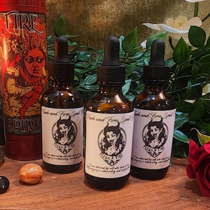 Peut inclure: Trois flacons en verre brun avec des compte-gouttes noirs et des étiquettes blanches qui indiquent "Flesh and Fire Spell". Les étiquettes présentent un graphisme d'une femme avec des cornes. Une bougie rouge avec un visage de femme est en arrière-plan.