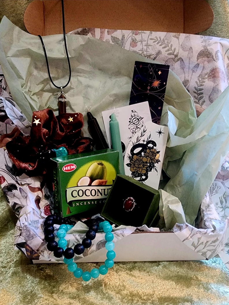 Puede incluir: Caja de regalo abierta con varios art&iacute;culos: collar, coletero, incienso, pulseras, anillo y tarjetas. La caja contiene una caja de incienso verde con el texto "Coconut Incense Co." y un anillo en una caja verde.