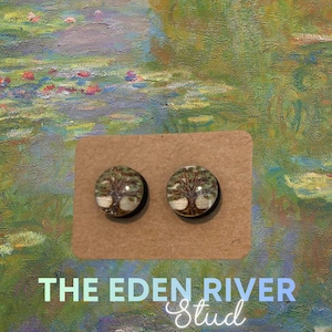 May include: Two round stud earrings featuring a tree design. The earrings are set on a brown card with the text "THE EDEN RIVER Stud" in a gradient font. The background is a colorful painting.