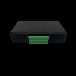 May include: A rectangular black storage case with a textured surface and a bright green plastic latch centered on the front edge. The case features a solid, opaque construction with a flat top and a secure locking mechanism for closure.