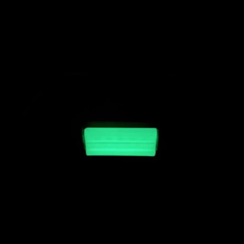 May include: A rectangular object emitting a bright, solid neon green glow against a completely black background. The light source appears uniform across the surface, creating a sharp, luminous horizontal bar shape that stands out in the darkness.