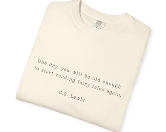 May include: A folded cream-coloured t-shirt featuring the quote "One day, you will be old enough to start reading fairy tales again." by C.S. Lewis, printed in black.
