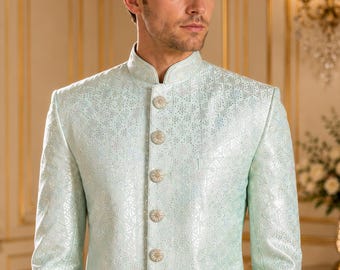 Puede incluir: Un sherwani de color verde menta claro con un sutil e intrincado patrón geométrico tonal en toda la tela. La prenda presenta un cuello alto tipo mandarín, mangas largas y una tapeta frontal asegurada con siete botones redondos plateados.