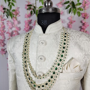 Pode incluir: Casaco creme com padr&atilde;o floral, usado por um manequim. O casaco &eacute; adornado com um colar de tr&ecirc;s fios com pedras preciosas verdes e uma moldura prateada. Um len&ccedil;o de bolso branco est&aacute; no bolso do peito.