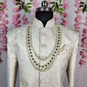 Pode incluir: Casaco creme estampado com gola mandarim e bot&otilde;es decorativos. Um colar de tr&ecirc;s fios com pedras preciosas verdes e detalhes prateados adorna o casaco. Um len&ccedil;o branco est&aacute; no bolso do peito. O casaco &eacute; exibido em um manequim.