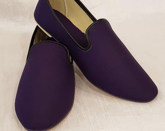 Op de afbeelding: Een paar paarse instappers. De schoenen hebben een ronde neus en een zwarte rand rond de opening. De binnenkant is lichtbeige van kleur. De schoenen zijn gemaakt van een gladde stof en worden op een witte ondergrond gepresenteerd.