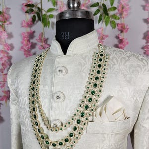 Pode incluir: Casaco creme com padr&atilde;o floral, adornado com um colar em camadas com pedras preciosas verdes. O colar &eacute; combinado com um len&ccedil;o de bolso a condizer. O casaco tem bot&otilde;es decorativos.