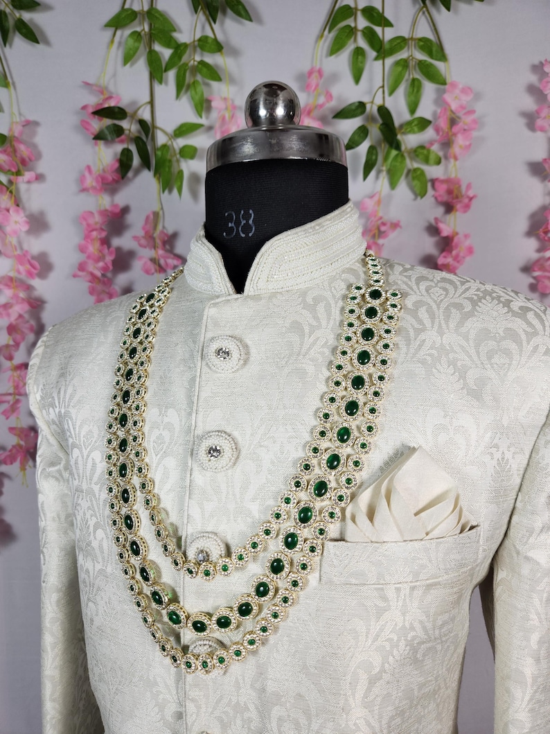 Pode incluir: Casaco creme com padr&atilde;o floral, adornado com um colar em camadas com pedras preciosas verdes. O colar &eacute; combinado com um len&ccedil;o de bolso a condizer. O casaco tem bot&otilde;es decorativos.