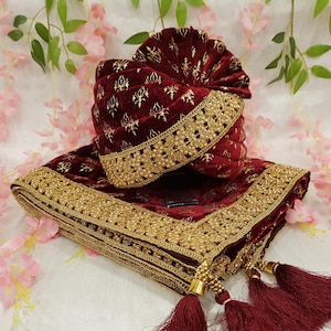 May include: A burgundy velvet turban and shawl set, featuring gold embroidery and beaded detailing. The turban is adorned with gold patterns and a beaded border. The shawl has a matching design, with gold tassels. This set is suitable for special events.