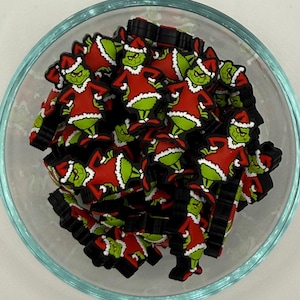 May include: A glass bowl filled with numerous small, colourful charms. Each charm features a green character wearing a red Santa suit with white trim and a matching hat. The charms are black around the edges.