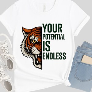Könnte beinhalten: Weißes T-Shirt mit einem Tiger-Grafik-Design in Orange, Schwarz und Weiß auf der linken Seite und dem grünen Text "YOUR POTENTIAL IS ENDLESS". Das T-Shirt wird mit hellblauen Jeans und grauen Turnschuhen kombiniert.