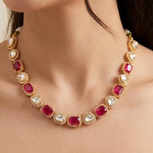 May include: A gold necklace and matching earrings set. The necklace has alternating ruby-red and clear, square-cut gemstones, each in a gold setting. The earrings have a similar design, with three gemstones.