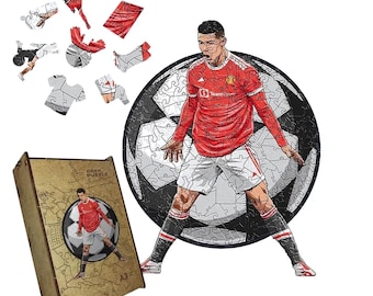 May include: A soccer-themed jigsaw puzzle featuring a player in a red jersey, set against a soccer ball background. The puzzle is partially assembled, with loose pieces scattered around. The puzzle box is visible.