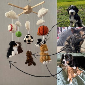 May include: A handmade baby mobile featuring crocheted elements. The mobile includes white clouds, a baseball, a green ball, a soccer ball, and an orange basketball. It also has crocheted figures of a dog and a cat.