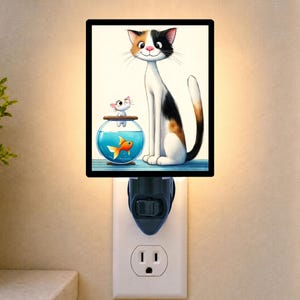 May include: A rectangular plug-in night light featuring a colorful illustration of a calico cat sitting beside a round glass fishbowl. Inside the bowl, a small orange goldfish swims, while a tiny white kitten sits on the rim of the bowl.