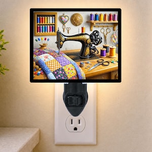 May include: A square night light featuring a printed scene of a black vintage sewing machine, a colorful patchwork quilt, spools of thread on a wooden shelf, scissors, and buttons. The night light has a black plastic base plugged into a wall outlet.