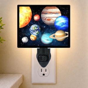 May include: A rectangular plug-in night light featuring a vibrant space scene with various planets, including Earth, Jupiter, and Saturn, set against a dark starry background. The light is plugged into a standard wall outlet and emits a soft glow.