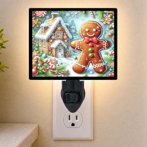 May include: A square plug-in night light featuring a festive holiday illustration of a brown gingerbread person with a red bow tie and green buttons, standing next to a snow-covered gingerbread house surrounded by candy canes and pine branches.