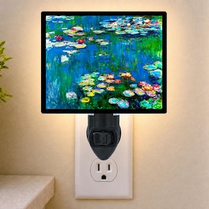 May include: A rectangular plug-in night light featuring a vibrant impressionist water lily painting with shades of blue, green, and pink. The light has a black frame and a black base with a manual toggle switch, plugged into a standard wall outlet.