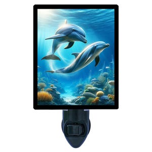 May include: A night light featuring a vibrant underwater scene with two dolphins swimming in a blue ocean. The image is framed in a black rectangular border, with a black base and a switch for easy use.