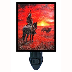 May include: Night light featuring a painting of a Native American on horseback, with a bison in the background, set against a fiery red and orange sunset. The night light has a black frame and a black plug.