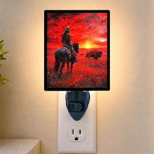 May include: A rectangular plug-in night light featuring a vibrant red and orange sunset scene. The image depicts a person in traditional headdress riding a horse across a grassy field, with a large bison standing nearby under a bright sun.